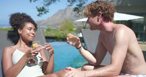 Young couple toasting by infinity pool on luxury resort deck, sipping lemon water
