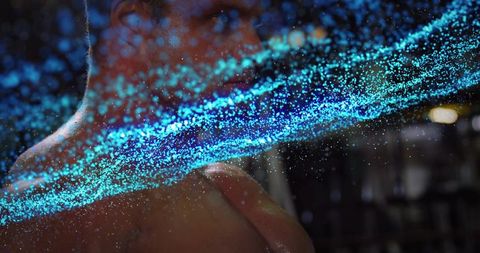 Glowing cyan particle stream veiling shirtless male torso in low light studio