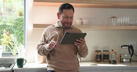 Mature Asian Man Reading Tablet in Bright Modern Kitchen with Coffee Maker and Green View
