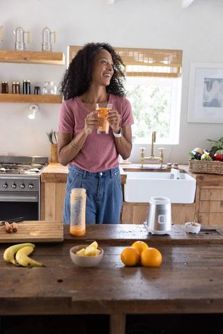 African american woman enjoying fresh orange juice in rustic sunlit kitchen with blender