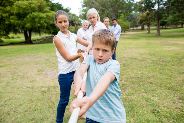 Multi-generation family engaging in a fun tug of war game in a park. Ideal for illustrating family bonding, teamwork, outdoor activities, and healthy lifestyle. Suitable for use in advertisements, articles, and promotional materials related to family events, outdoor recreation, and community gatherings.