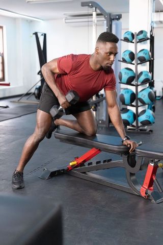 African american man performing one-arm dumbbell row on adjustable bench in modern gym