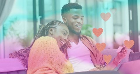 Happy Couple Relaxing on Couch Looking at Smartphone with Heart Graphics