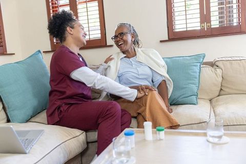 Home caregiver sharing warm conversation with senior african american woman on couch