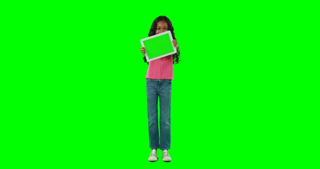 A young girl holds a tablet with a green screen on a solid green background. This can be used for technology advertisements, educational materials, and digital device promotions. Ideal for mockups, showcasing app interfaces, or interactive content.