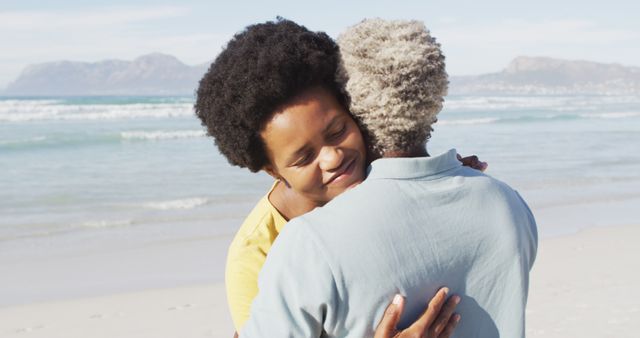 This image shows an affectionate couple embracing on a scenic beach with a beautiful ocean view. Ideal for use in marketing campaigns promoting travel, vacation destinations, or highlighting themes of love and diversity. Suitable for websites, brochures, and social media posts focusing on relationships, wellness, and adventure.