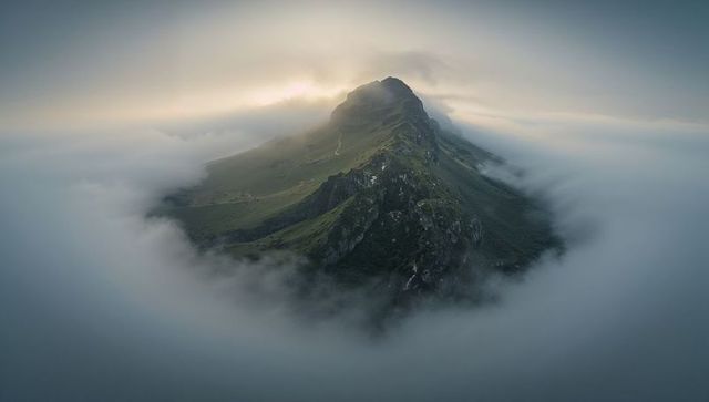 Rising narrow mountain ridge cutting through sea of clouds with winding trail at sunrise