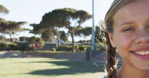 Smiling young girl with braid on sunlit turf field, lens flare, outdoor youth portrait, copy space
