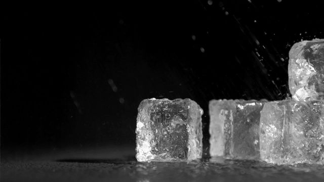 This video shows rain droplets splashing on ice cubes against a dark background in slow motion. Suitable for illustrating concepts related to freshness, cold beverages, summer, and hydration. Great for use in advertisements of cold drinks, ice, freezer, or air conditioning products. Can also be used in creative projects needing high-contrast and dramatic effect images.