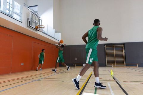 Male basketball players practicing jump shot in indoor gym wearing green uniforms