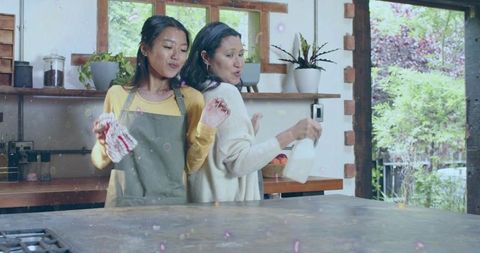 Mother and daughter dancing at sunlit kitchen island with plants and wooden accents