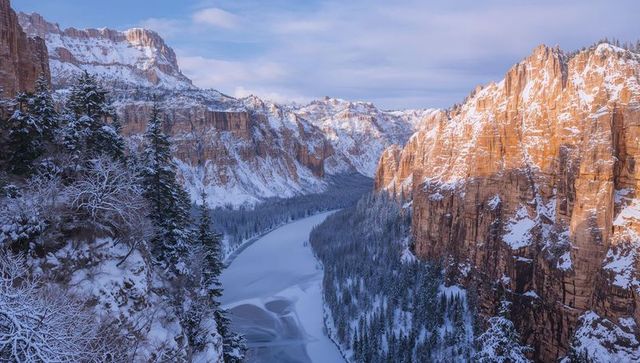 Sunlit red cliffs winding frozen river through snow-covered canyon at sunrise