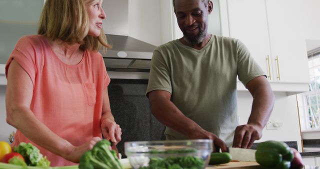 Happy diverse senior couple chopping vegetables in kitchen and talking. staying at home in isolation during quarantine lockdown.