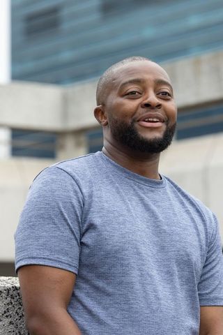 African man leaning on concrete barrier smiling and looking right in urban blue t-shirt