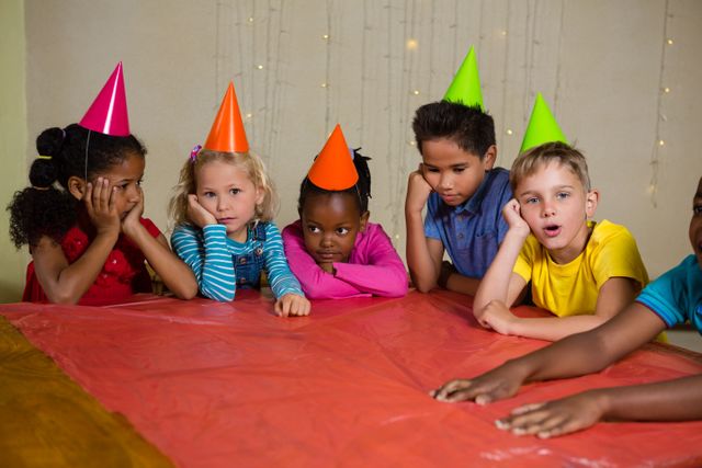 Bored children in part hat sitting at table during birthday