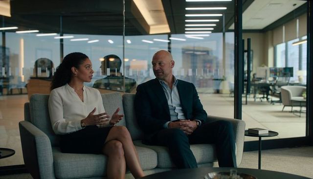 Executives discussing strategy, gesturing and listening in glass-walled office lounge