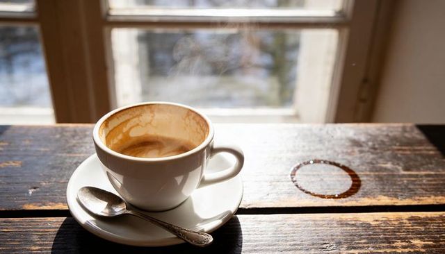 Steaming espresso cup with crema and coffee ring on rustic wooden table