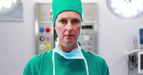 Female surgeon standing in or wearing green scrubs with surgical mask around neck