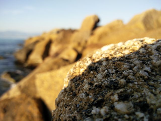 Close-up of rocky coastline capturing the intricate texture of rocks with the golden hue of sunset. This image is perfect for nature-themed publications, travel brochures, or inspirational background illustrations emphasizing raw natural beauty.