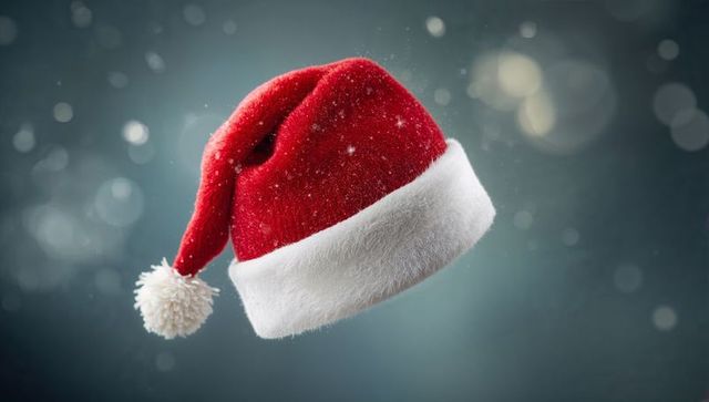Floating velvet Santa hat dusting with snowflakes against teal bokeh holiday background