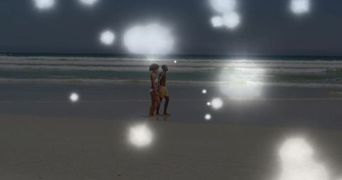 Couple walking shoreline at twilight with dreamy lens flare glow over ocean