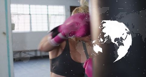 Mid-adult woman boxing workout hitting heavy bag wearing pink gloves gym studio