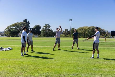 Young men playing casual cricket on sunny park field demonstrating teamwork and fun