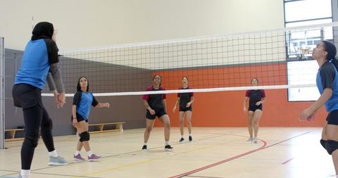 Female volleyball players competing at net in indoor gym court showing teamwork and motion
