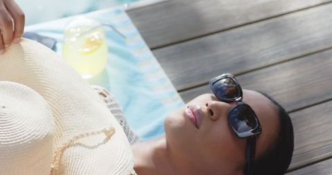 African american woman relaxing on sunlit deck with straw hat and lemonade