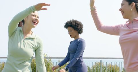 Diverse women stretching on rooftop terrace with ocean view in colorful activewear