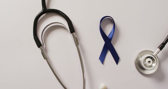 Blue ribbon placed alongside stethoscope and medical tools on white background. Represents health awareness campaigns such as diabetes, colon cancer, or men's health. Useful in health awareness materials, medical articles, educational posters, and healthcare services promotions.