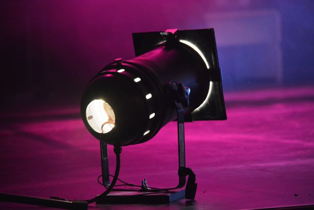This image shows a close-up view of a stage spotlight with vibrant purple and magenta background lighting. It is ideal for use in materials related to theatre productions, concerts, events, performances, and shows. It can be used in marketing and promotional content or blogs discussing event planning and stage equipment.