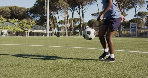 African american teen juggling soccer ball on sunny artificial turf near sideline