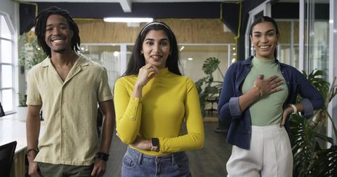 Smiling diverse team posing in modern open-plan office with plants and smartwatches