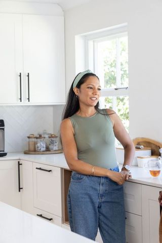 Casual woman leaning on white kitchen counter in modern bright minimalist home interior