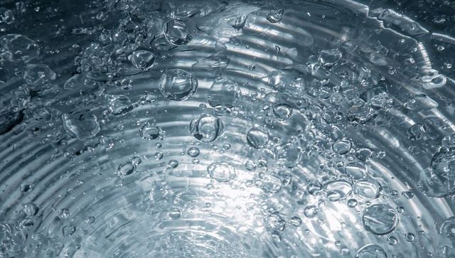 Floating air bubbles creating concentric ripples in ribbed glass tube with blue backlit reflections