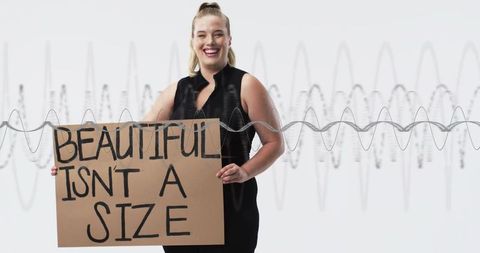 Plus-size woman holding sign 'beautiful is not defined by size' smiling for body positivity campaign