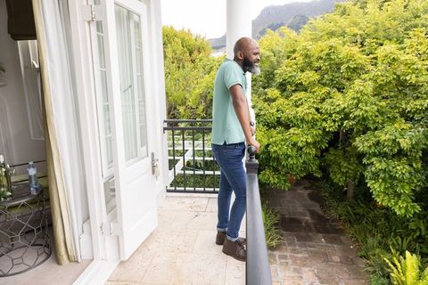 Mature african american man enjoying peaceful garden view from balcony leaning on railing