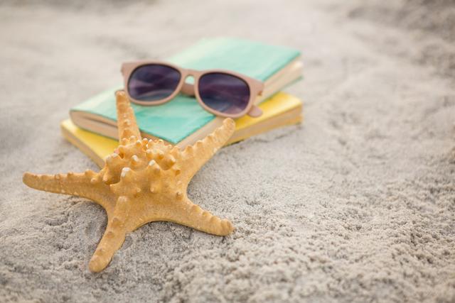 Starfish lying on sandy beach next to sunglasses and books. Ideal for promoting summer vacations, beach holidays, and relaxation. Perfect for travel blogs, vacation brochures, and leisure-themed advertisements.