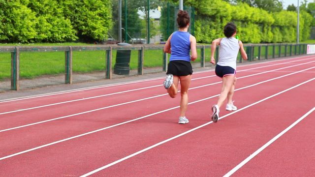 Two women are actively participating in a relay race on an outdoor track. This captures the dynamics of teamwork in athletics. Useful for illustrating fitness endeavors, motivational content, athletic training facilities, or promotional materials for sports events.