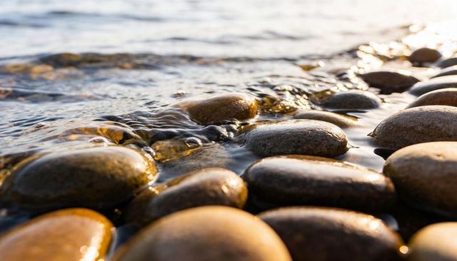 Glowing wet pebbles reflecting low sunlight at water edge with gentle ripples and glossy stones