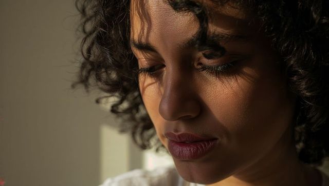 Contemplative woman gazing in warm window light, closeup portrait with textured skin
