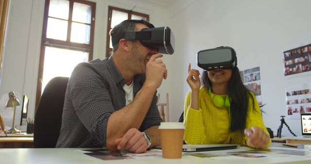 Two young professionals are immersed in a VR experience at their workspace. They appear engaged and happy, highlighting the fun and collaborative aspects of modern technologies. Suitable for use in articles or advertisements related to workplace innovation, team building, or cutting-edge technology in business environments.