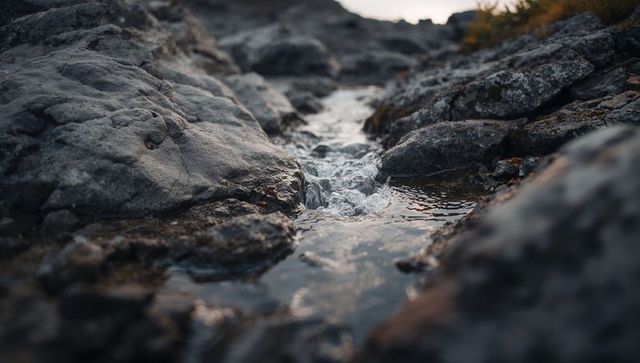 Flowing narrow rivulet cutting grey rock outcrop with cascading pool and wet lichen