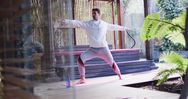 Man engaged in yoga in a serene outdoor environment with plants and wooden deck. Ideal for promoting wellness, fitness, and healthy lifestyle concepts. Suitable for content related to exercise routines, relaxation techniques, and mindful living.