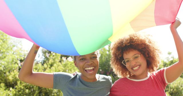 Happy diverse lesbian couple embracing and holding a rainbow flagoutdoors. Togetherness, relationship, love, lgbtg awareness summer and nature, unaltered.