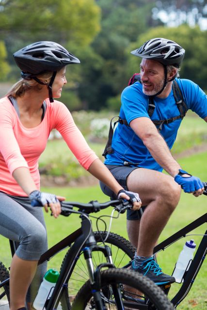 This image shows a smiling athletic couple riding bicycles outdoors, wearing helmets and sports attire. Ideal for promoting active lifestyles, fitness programs, outdoor activities, and healthy living. Can be used in advertisements, blogs, and social media posts related to cycling, sports, and adventure.