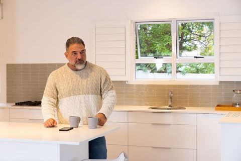 Man in cozy cable-knit sweater at modern white kitchen island with mugs and smartphone