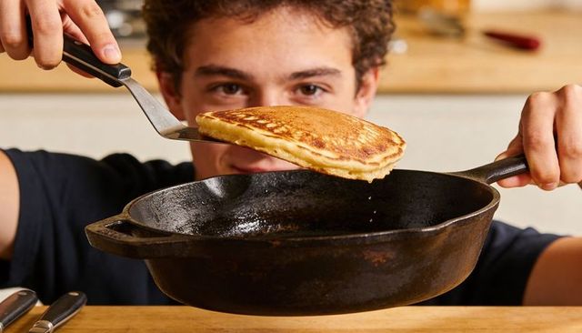 Adolescent Flipping Golden Pancake in Cast-Iron Skillet Closeup Home Kitchen Breakfast