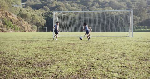Children playing soccer on grassy field kicking ball towards goal